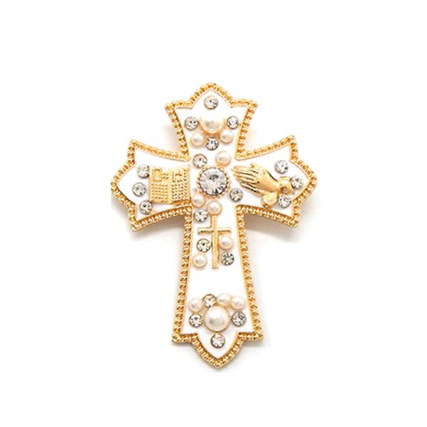 AN ELABORATE CROSS BROOCH FEATURING PEARL AND CRYSTAL ACCENTS SET AGAINST A DARK BACKGROUND WITH RELIGIOUS SYMBOLS